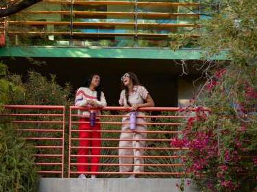 Two people stand on a vine-covered balcony while holding beautiful Stanley water bottles